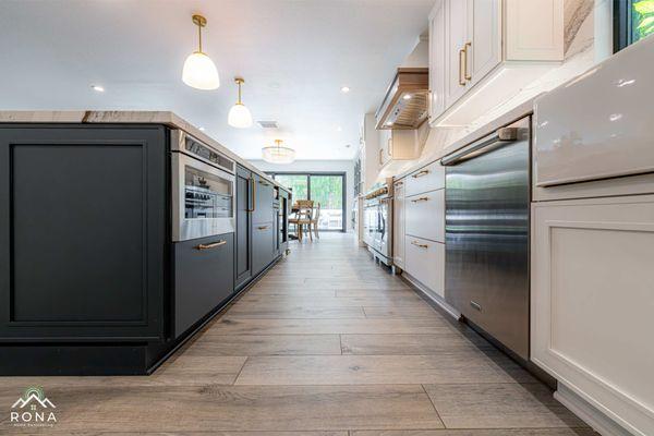 Long kitchen view with dark cabinets, appliances, and wood flooring.