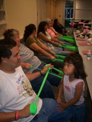 A participant father doing Dyna band exercises while his daughter looks on.