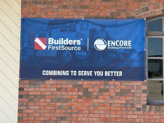 A large banner displayed on a brick wall with the logos of Builders FirstSource and Encore Building Products...