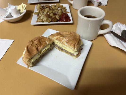 Sausage, egg and cheese on a hard roll breakfast, home fry potatoes and coffee.