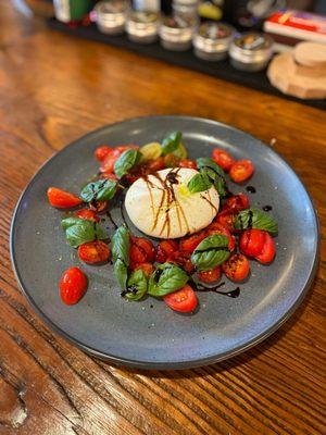 Burrata Caprese with balsamic reduction, tomatoes, and basil.