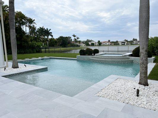Swimming pool renovation in Palm Beach Gardens features pebble surface, new spa, marble pavers, landscaping, artificial turf.