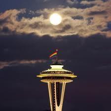 The Space Needle flying the Pride Flag under the full moon.