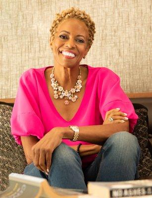 Smiling woman portrait. Seated on couch, wearing pink shirt and jeans.