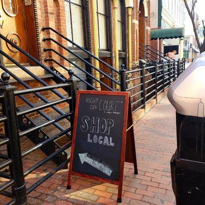 Sidewalk just outside with sign leading you to stairs up to store