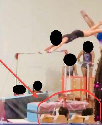 see red arrow pointing to coach Kimmy who is eating and chatting. She's supposed to be spotting and helping with high level bar skills.