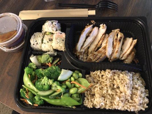 Bento box with chicken, brown rice, veggies, and California rolls.