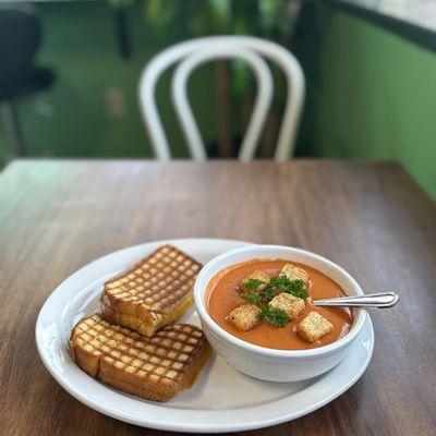 Warm tomato basil soup with croutons and fresh parsley, served with a classic grilled cheese for a simple and comforting bite.