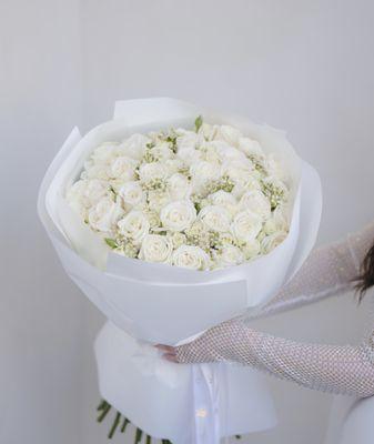 A full bouquet of fresh white roses, paired with delicate filler flowers and wrapped in matching white paper. A timeless and elegant choice