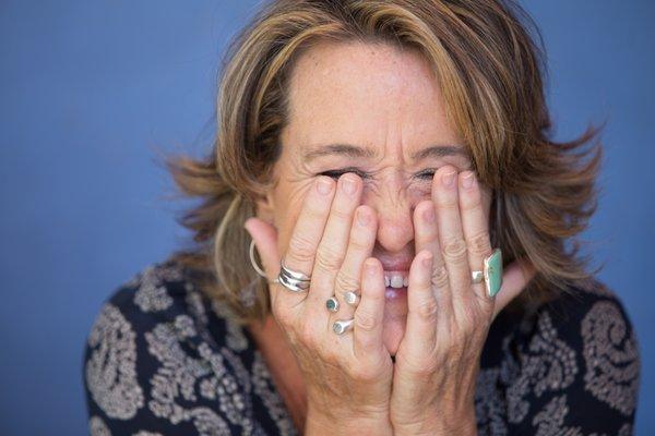 Working actor and long-time coach Lauren Letherer, laughing and covering her eyes with hands covered in bohemian rings. Blue background.