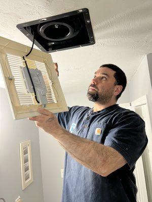 Electrician applying the finishing touch by install the grille to a newly bath exhaust fan.