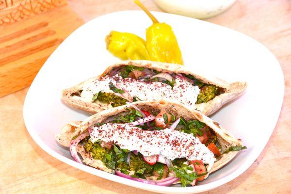 Homemade falafel patties stuffed in a freshly baked pita filled with coconut-tzatziki sauce, lemon-tahini, and a salad of Parsley, Mint, Red