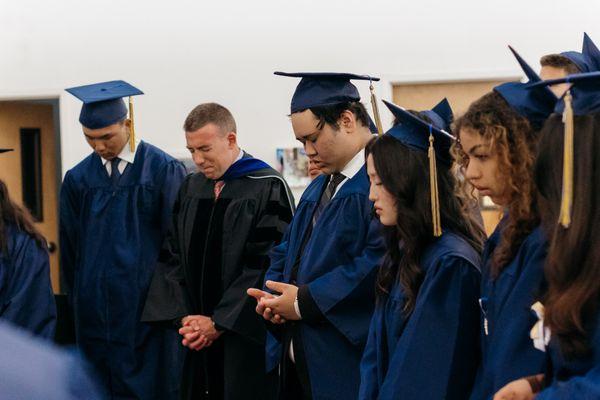 Faculty and students in prayer before graduation. Picture courtesy of Breanna Rhea Photography.