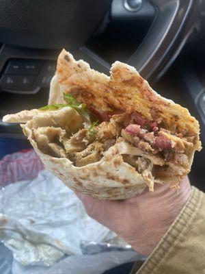 Chicken shwarma sandwich with pickled onions, some lettuce, white and hot sauce.