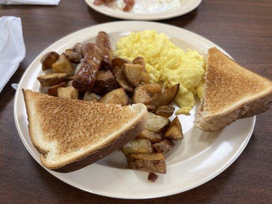 Breakfast platter with scrambled eggs, home fries, sausage links and toast.