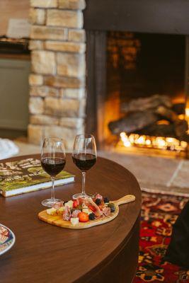 Cozy fireside charcuterie at The Parlor at Vinarosa--two glasses of red wine and artisan bites by the warm stone fireplace.