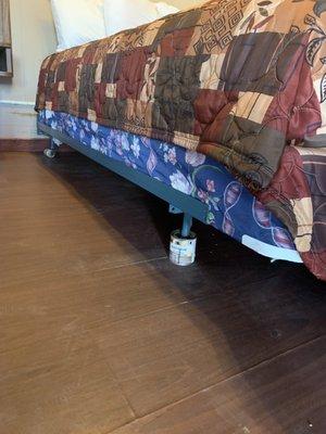 A paint can holding the corner of the bed up.