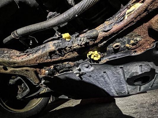 severely damaged vehicle frame and suspension system that's rusted and rotting and where holes were injected with expanding foam