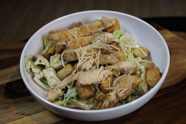 A freshly grilled chicken breast atop chopped romaine lettuce, tossed with parmesan cheese, croutons, and caesar dressing