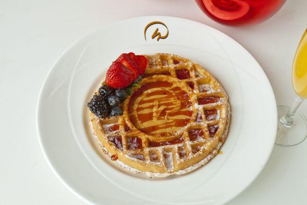 A plated waffle with powdered sugar, syrup, strawberries, blueberries, and blackberries with the Rosen Hotels & Resorts insignia on it