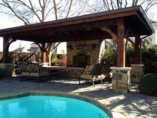 Covered structure with natural stone fireplace and interlocking paver pool deck/seating area