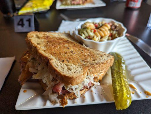 Reuben sandwich with pasta salad and a pickle.