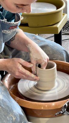 Sarah demonstrating throwing a cylinder with clay during pottery class.