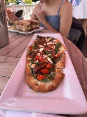 #2 flatbread with goat cheese, bacon, hot honey, peppers, and arugula.