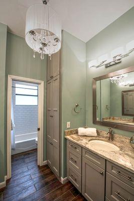 Elegant hall bathroom remodel from the 1970s.  Granite, silk and crystal chandelier, white subway tile, wood look porcelain flooring.