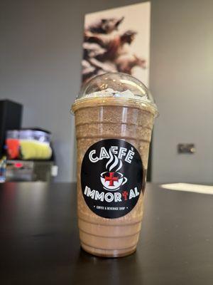 A blended coffee drink at Caffè Immortal with a portrait of Jesus, and a slushee machine in the defocused background.