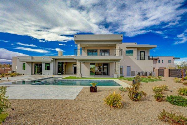 Modern desert showpiece: clean lines, floor-to-ceiling glass, and seamless indoor-outdoor living. Resort backyard with pool.