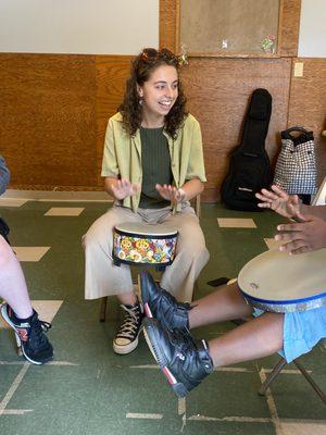 A music therapist is playing a drum and interacting with participants.