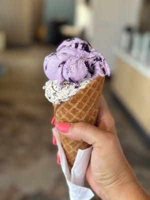 Ube cookie split scoop with cookies and cream in a waffle cone