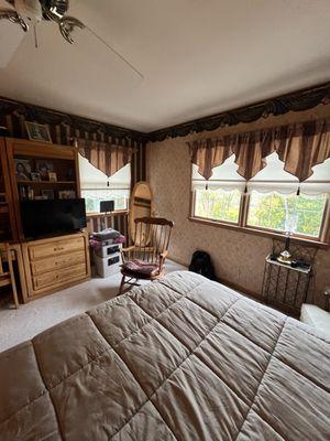Before photo of the bedroom featuring wallpaper and a decorative crown border, showing the space prior to the transformation.