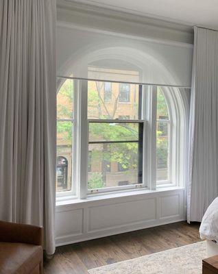 Arch windows covered with a Sunscreen and soften with blackout drapery