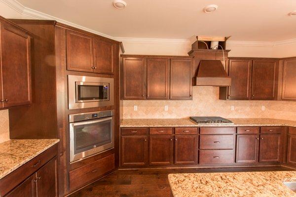 True gourmet kitchen with vented hood, cooktop, island and buil in mircowave and oven