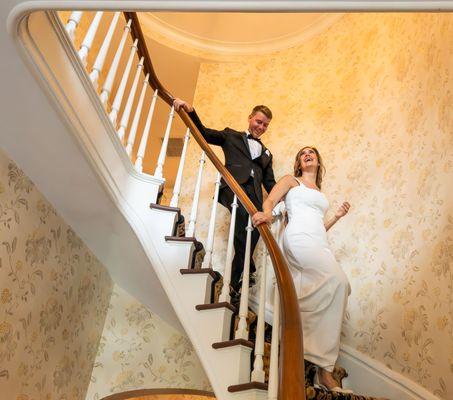 Joyful newlyweds Chad and Melissa descend elegant staircase at Hannum House, Sherwood Inn, Skaneateles Lake, NY.