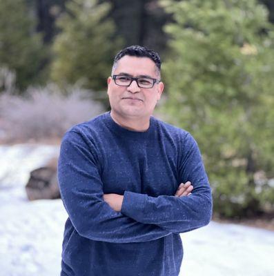 pose , blue sweater , wearing black glasses , background is snow and trees