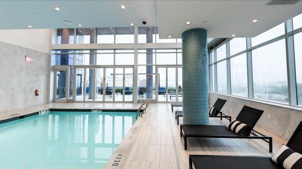 A bright, modern indoor pool amenity features floor-to-ceiling windows and access to an outdoor deck.