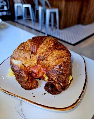 Breakfast Croissant Sandwich with scrambled eggs, cheddar cheese, bacon, tomato, lettuce, aioli.