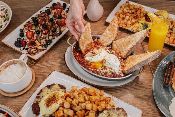 A delicious brunch table featuring poached eggs shakshuka, French toast, pancakes, and crepes at your go-to breakfast near you.
