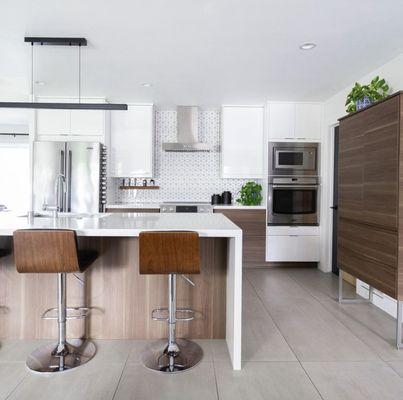 Modern kitchen with white cabinets, stainless steel appliances, island with stools, geometric backsplash, and plants for a cozy, sleek vibe