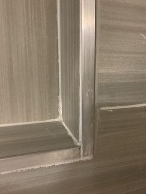 "Clean finish" with an uneven metal frame, sloppy caulking and chipped tile due to poor craftsmanship while cutting.