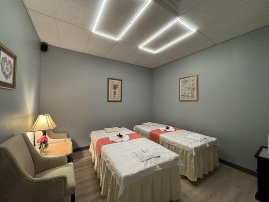 Spacious couples massage room featuring two cozy tables, warm lighting, and tranquil décor for a shared wellness experience.