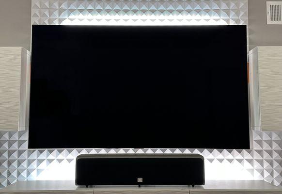 LG OLED TV mounted among decorative acoustic panels and media storage cabinets