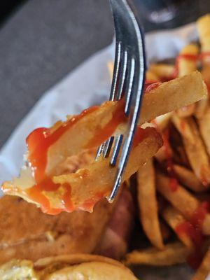 A fork holding a French Fries with ketchup.