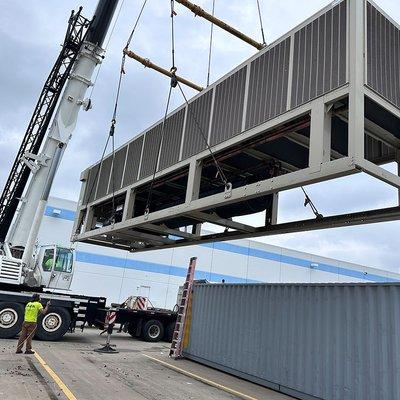 Huge crane lifts large HVAC unit onto warehouse rooftop.