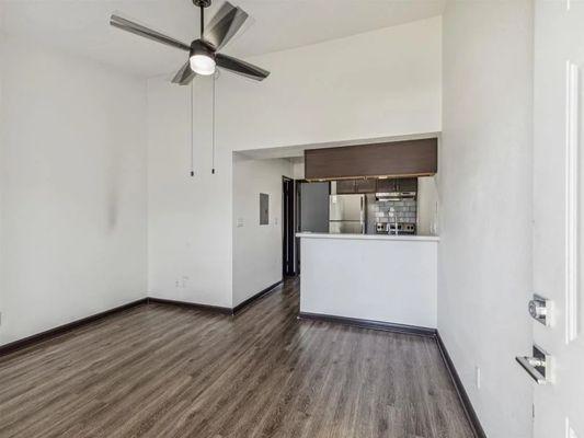 An empty living room with a kitchen and a ceiling fan
