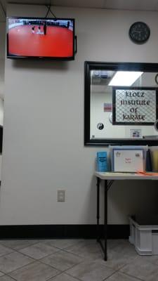 TV so you can watch class from the lobby. Background is the main office. Table has check-in cards and other information.