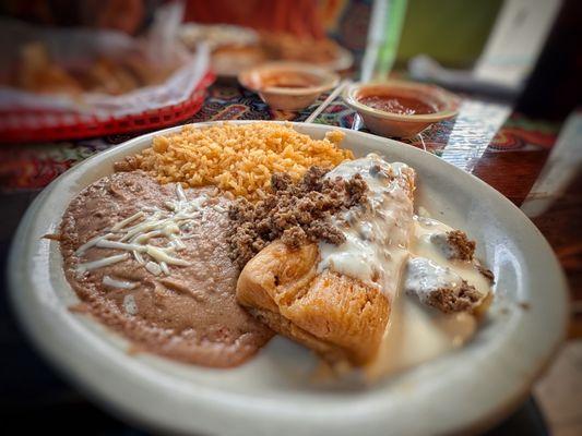 Lunch Tamal A pork tamale covered with cheese sauce and chunks of ground beef.